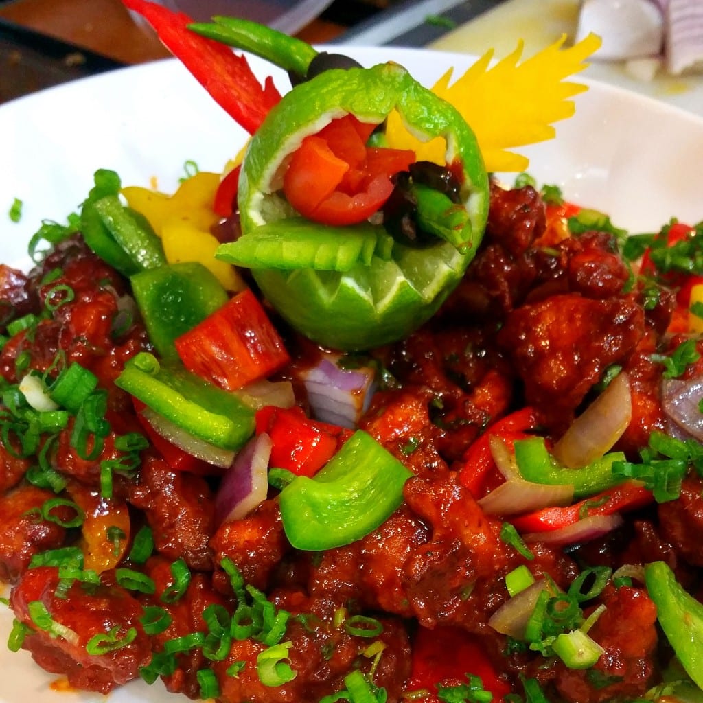 A large IndAroma platter of Indo-Chinese chilli chicken finished with peppers, red onion and spring onion.